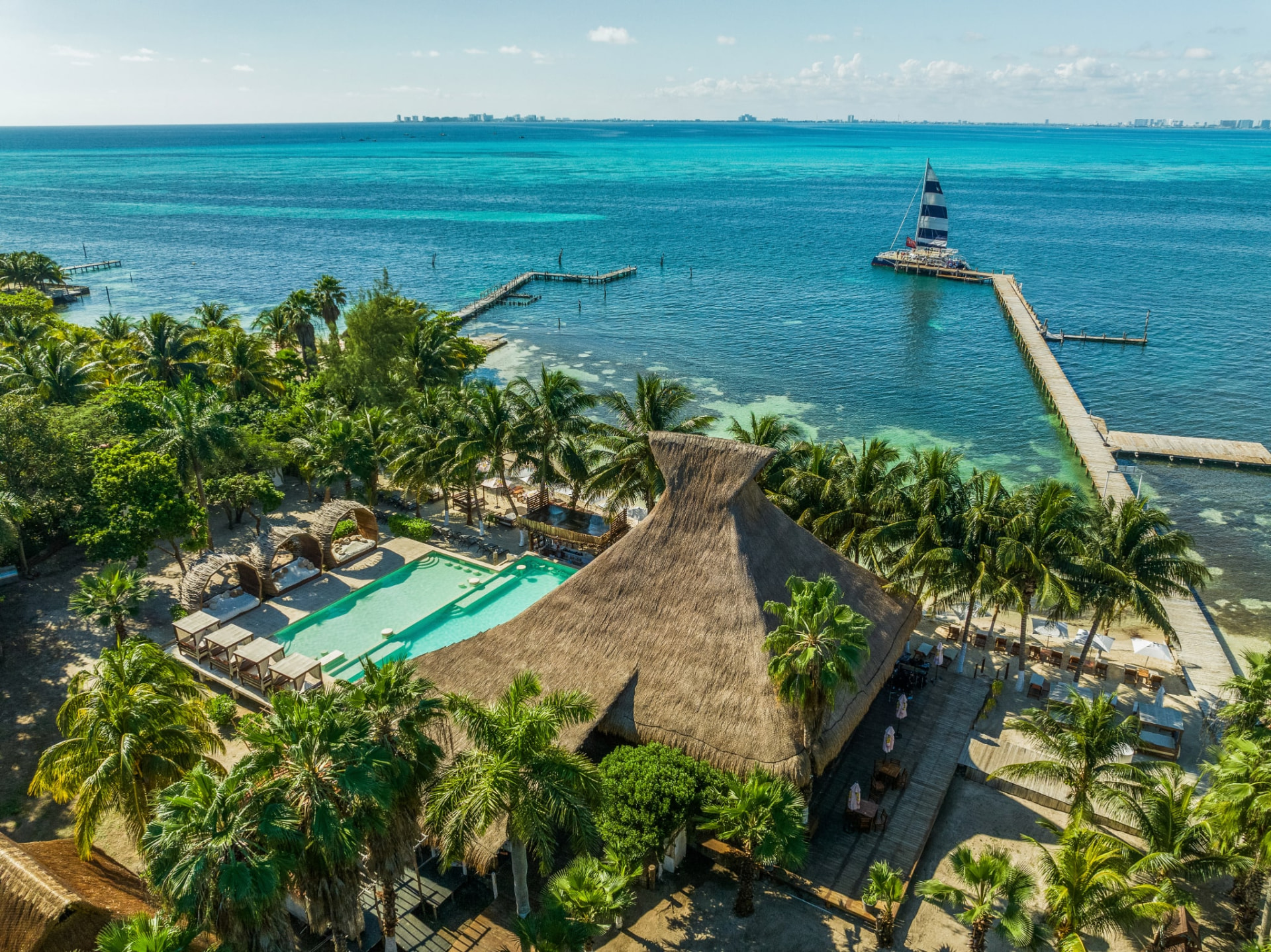 Vista aérea de un club de playa en la Riviera Maya con palapa, piscina, muelles y mar turquesa